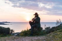 Homme assis avec guitare sur la côte — Photo de stock