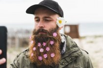 Homem com flores na barba tomando selfie — Fotografia de Stock
