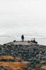 Вид сзади человека с камерой, стоящей на пирсе против снежного хребта в тумане, Исландия. — стоковое фото