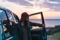 Uomo in cappello in piedi in auto al mare — Foto stock