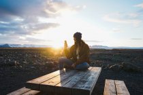 Woman sitting on wooden table at sunset — Stock Photo
