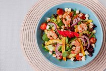 Vegetable salad with shrimps in blue bowl on mat — Stock Photo
