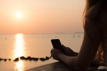 Mujer con teléfono inteligente de pie en la playa - foto de stock
