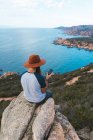 Человек в шляпе сидит на скале у моря — стоковое фото