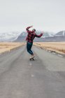 Vue arrière de hipster guy équitation skateboard sur route longue pavée avec des montagnes enneigées sur fond en Islande. — Photo de stock