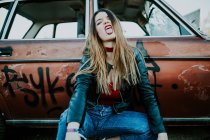 Attractive glamour woman looking at camera and showing tongue out while sitting at grungy vintage car. — Stock Photo