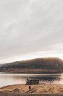 Paisaje de lago remoto y casa en la costa con el hombre caminando solo en la puesta del sol, Islandia. - foto de stock