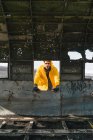 Beau jeune homme en veste jaune debout à l'extérieur de la carcasse de l'avion abandonné et regardant la caméra tout en voyageant à travers l'Islande — Photo de stock