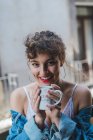 Кучерява жінка з чашкою кави на балконі — стокове фото