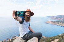 Fröhlicher Mann macht Selfie auf Felsen — Stockfoto