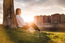 Frau sitzt unter Baum im Sonnenlicht — Stockfoto