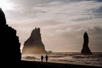 Силуэт людей на берегу со скалами — стоковое фото