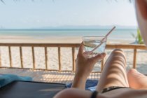 Женщина со стаканом воды расслабляющая на берегу моря — стоковое фото