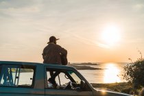 Чоловік сидить на даху автомобіля на морі — стокове фото