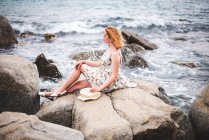 Redhead woman sitting on rock at ocean — Stock Photo