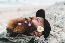 Homem com flores na barba deitado — Fotografia de Stock