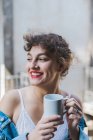 Curly woman with cup of coffee on balcony — Stock Photo