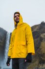 Mann in gelbem Regenmantel steht am Wasserfall — Stockfoto