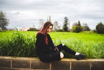 Frau sitzt auf Ziegelmauer im Grünen — Stockfoto