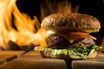 Вкусный бургер с большой кашей, лежащий на деревянном столе на фоне огня — стоковое фото