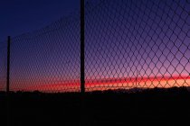 Silhouette di vista vicino alla città sul tramonto attraverso una recinzione — Foto stock