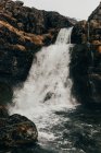 Waterfall flowing from gloomy black rocks — Stock Photo