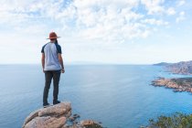 Uomo in cappello in piedi sulla roccia al mare — Foto stock