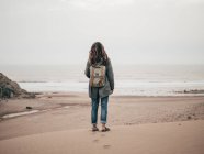 Woman with backpack standing at ocean — Stock Photo