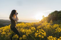 Femme prenant des photos avec des fleurs jaunes — Photo de stock