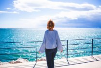 Woman standing at handrail and looking at ocean — Stock Photo