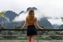 Frau lehnt sich in Geländer und blickt auf Berge — Stockfoto