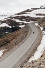 Aerial view of traveler riding skate on long remote road in snowy mountains of Iceland. — Stock Photo