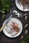Сырые креветки и рыбное филе, подаваемые на тарелке на черной поверхности — стоковое фото