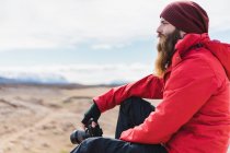 Man with camera sitting in barren land — Stock Photo