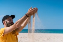 Homem derramando areia na praia — Fotografia de Stock