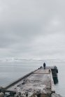 Uomo in piedi sul molo di pietra bagnata nel mare scuro con nuvole cupe sopra, Islanda. — Foto stock