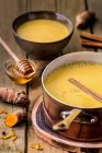 Pot full of appetizing yellow soup with honey on wooden table. — Stock Photo