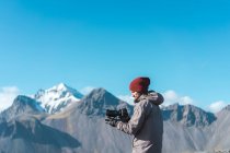 Seitenansicht eines bärtigen Mannes mit Hut, der eine Kamera mit professionellem Objektiv hält und in Island wegschaut — Stockfoto