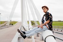 Hipster sitzt auf Brückengeländer — Stockfoto