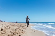 Femme courant le long de la plage de sable — Photo de stock