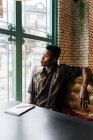 Hombre negro sentado en la mesa en la cafetería - foto de stock