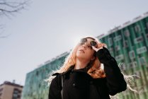 Élégante jeune rousse femme en lunettes de soleil debout en ville — Photo de stock