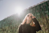 Стильная молодая рыжая женщина в солнцезащитных очках, стоящая в городе — стоковое фото
