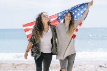 Zwei junge erwachsene Frauen posieren am Strand mit US-Flagge. — Stockfoto