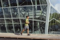 Homem étnico jogging contra edifício moderno na cidade — Fotografia de Stock