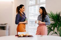 Mulheres muito jovens de pé juntos e falando sobre coffee break no escritório. — Fotografia de Stock