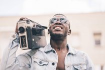 Усміхнений чорний чоловік в сонцезахисних окулярах ходить з старовинним радіопристроєм — стокове фото