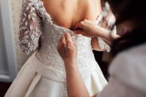 Mano ayudando a la novia irreconocible a botón vestido blanco. - foto de stock