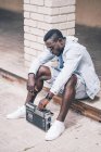 Чорний чоловік сидить на підлозі з старовинним радіопристроєм — стокове фото