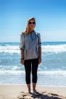 Donna in occhiali in piedi sulla spiaggia — Foto stock